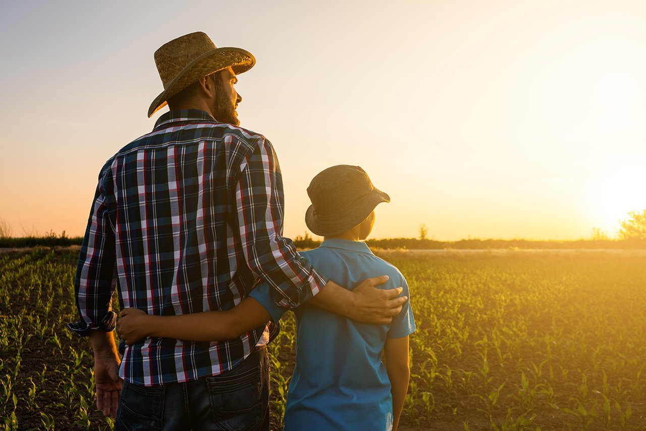farmer with his arm around his son's shoulder looking at the sunset across their Nebraska field, discussing their Legacy Plan